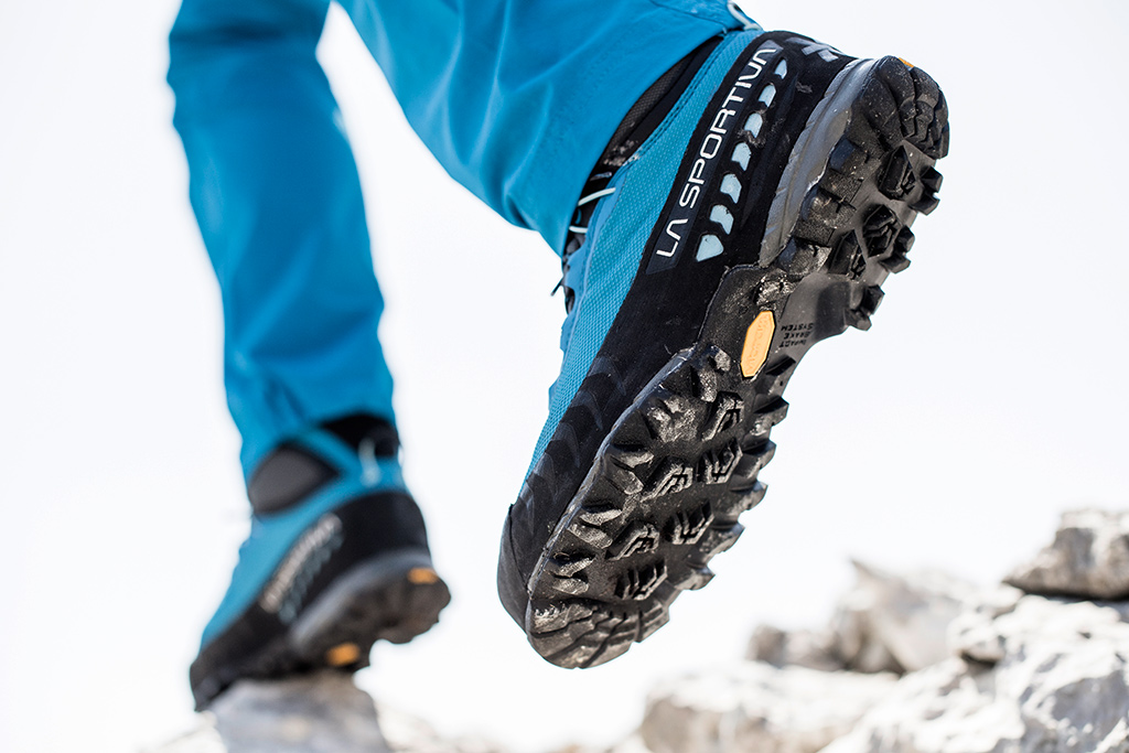 Damskie buty trekkingowe w akcji - zbliżenie na podeszwę Vibram. Nogi w niebieskich spodniach oraz wysokie buty w góry o niebieskiej cholewe
