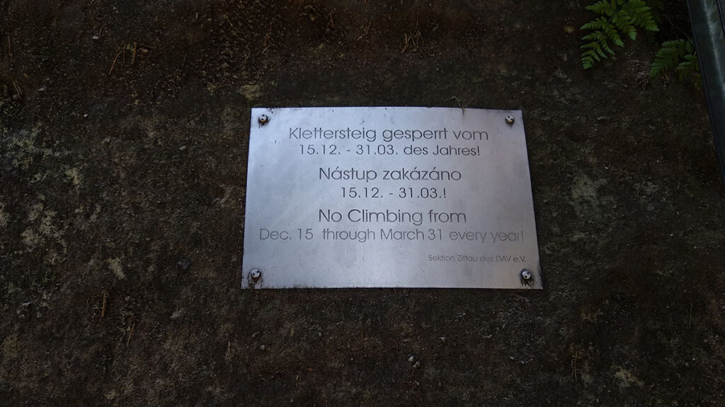 tabliczka przytwierdzona do skały z napisami w j. niemieckim, czeskim i angielskim informującym o zakazie wejścia w okresie od 15 grudnia do 31 marca każdego roku