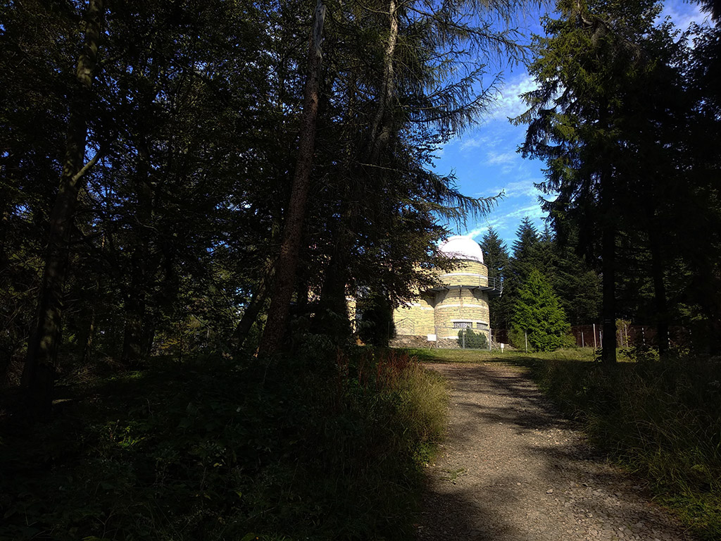 Droga przez las, na której końcu widać budynek zwieńczony kopułą - charakterystyczny kształt obserwatorium astronomicznego