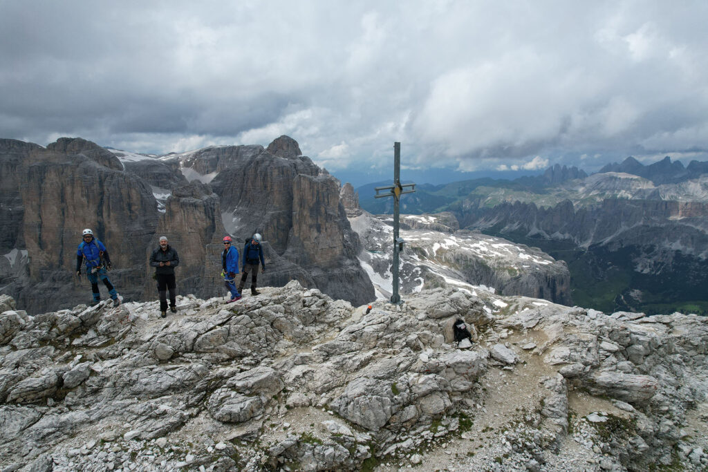 Cztery osoby na szczycie, obok metalowy krzyż, w tle widoczne bliższe i dalsze szczyty gór
